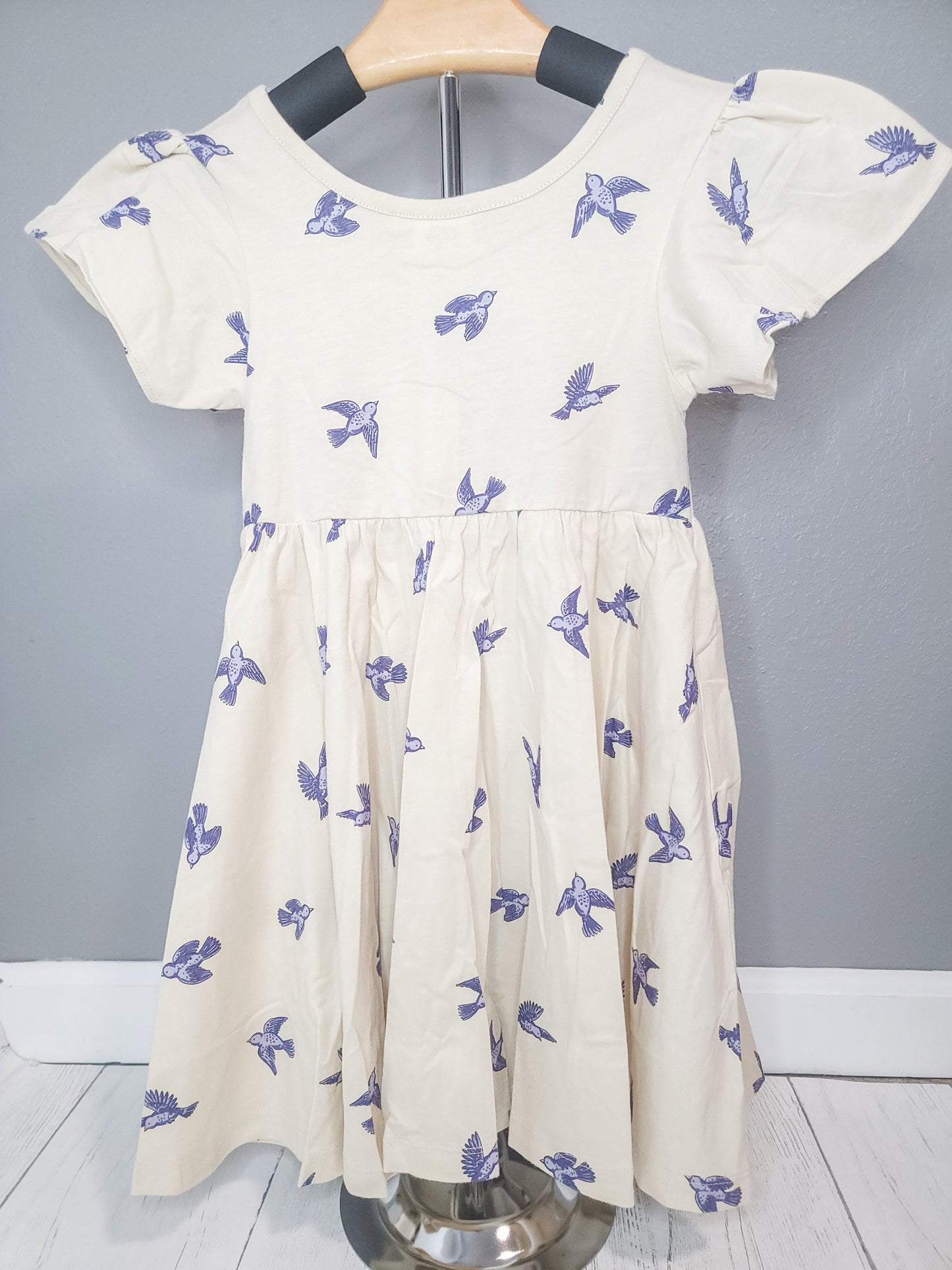 Bluebird Twirl Dress for toddler girls displayed on clothing rack, showing full cotton dress design and twirl-friendly fit