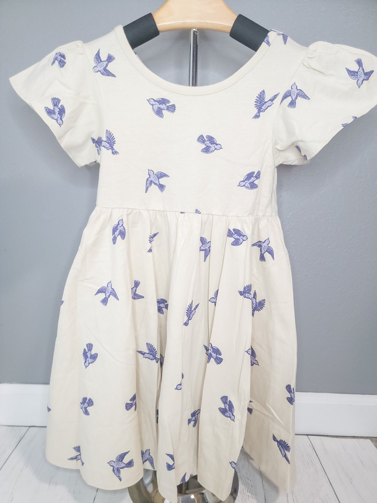 Full view of Bluebird Twirl Dress for toddler girls on rack, highlighting cotton fabric and flutter sleeves