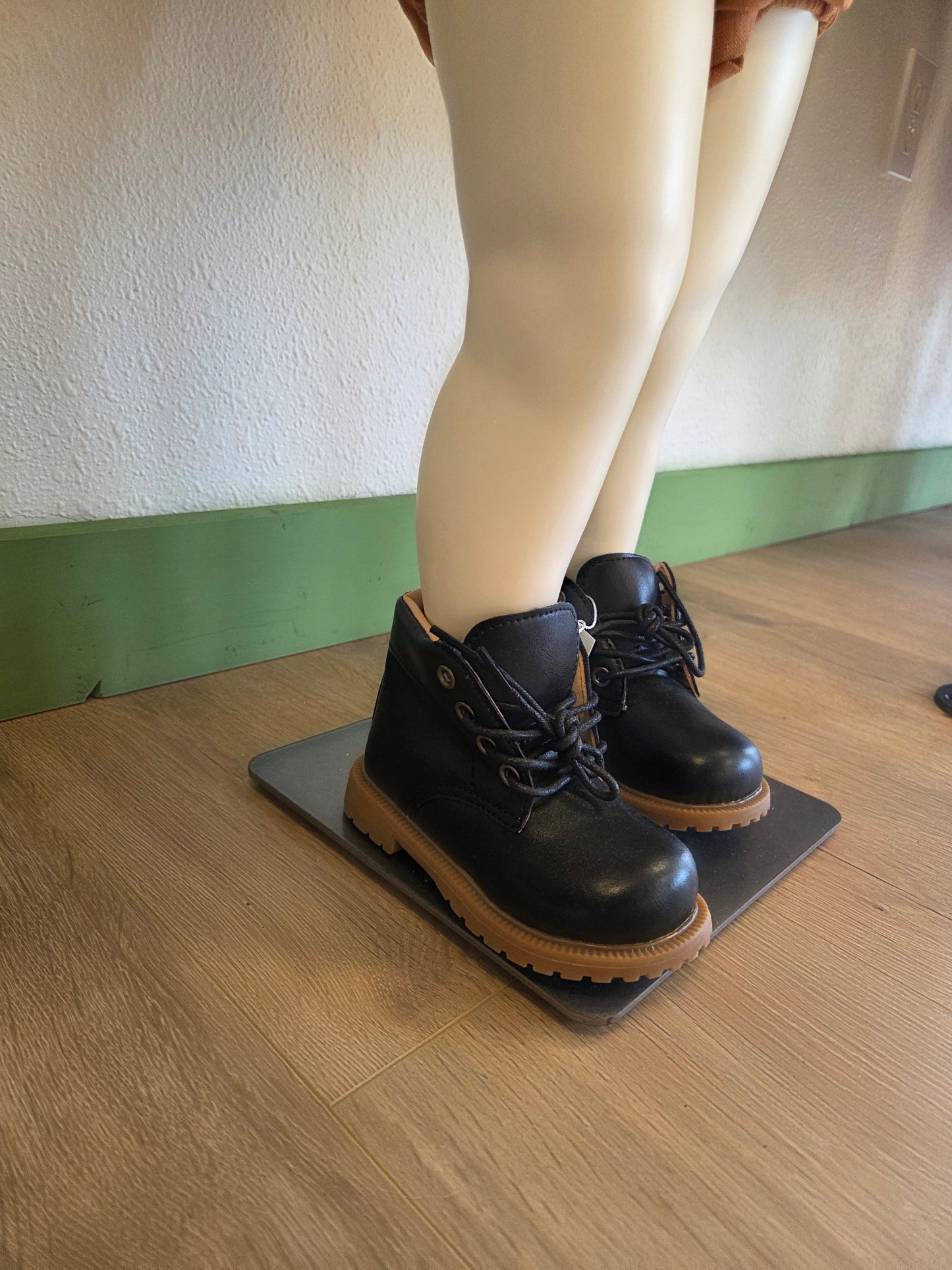 Side view of black unisex toddler and youth combat boots on mannequin, showing silhouette and lace-up detail