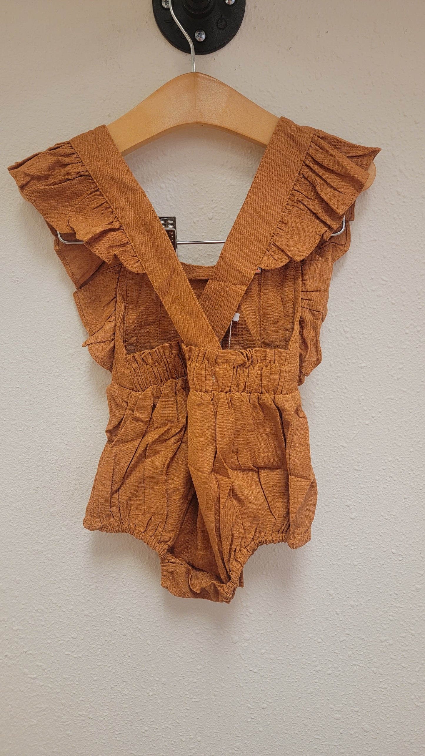 Eleanor Embroidered Romper hanging on display, back view, caramel linen with floral embroidery and ruffle detail