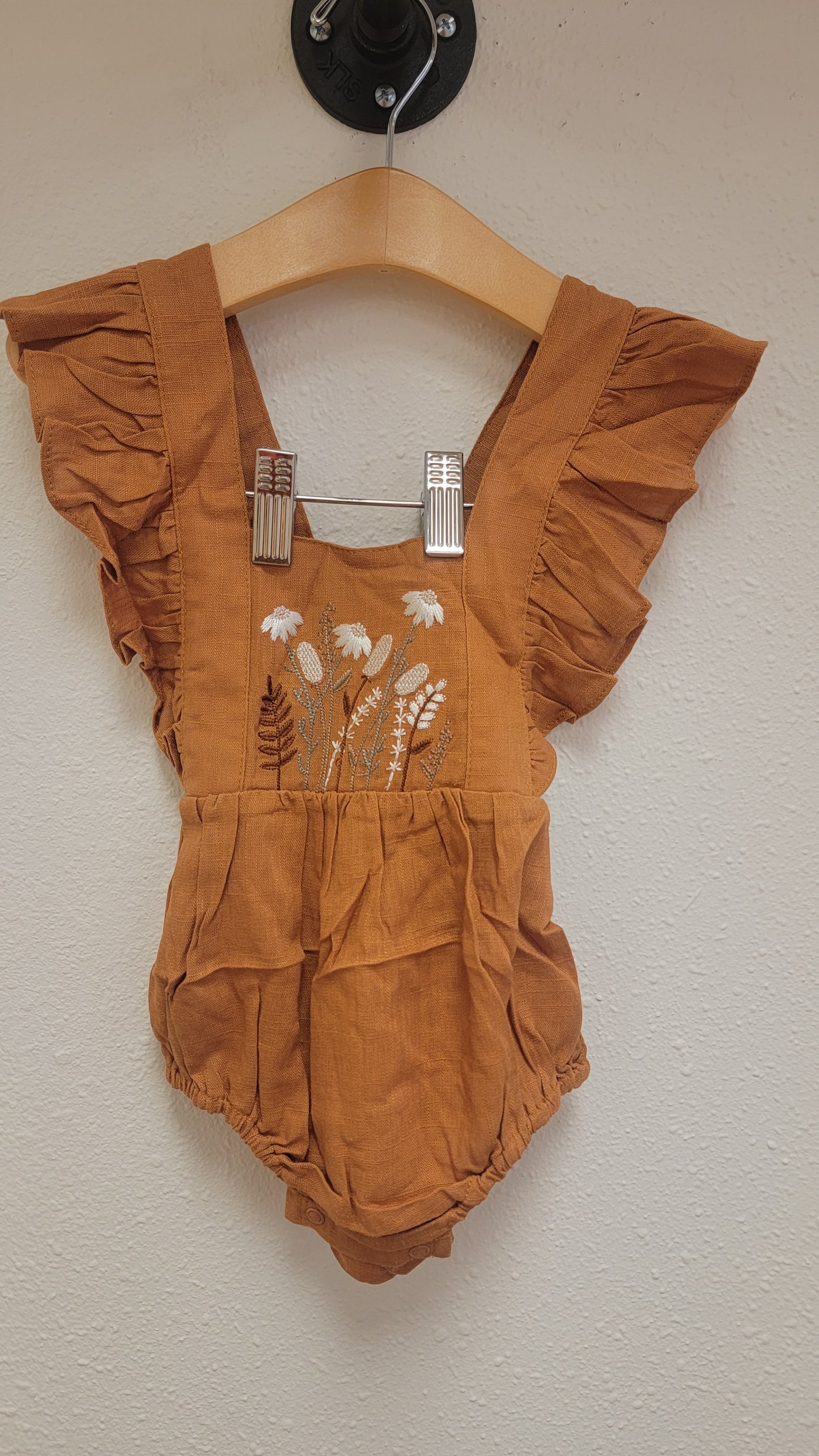 Eleanor Embroidered Romper hanging on display, front view, caramel linen with floral embroidery and ruffle detail