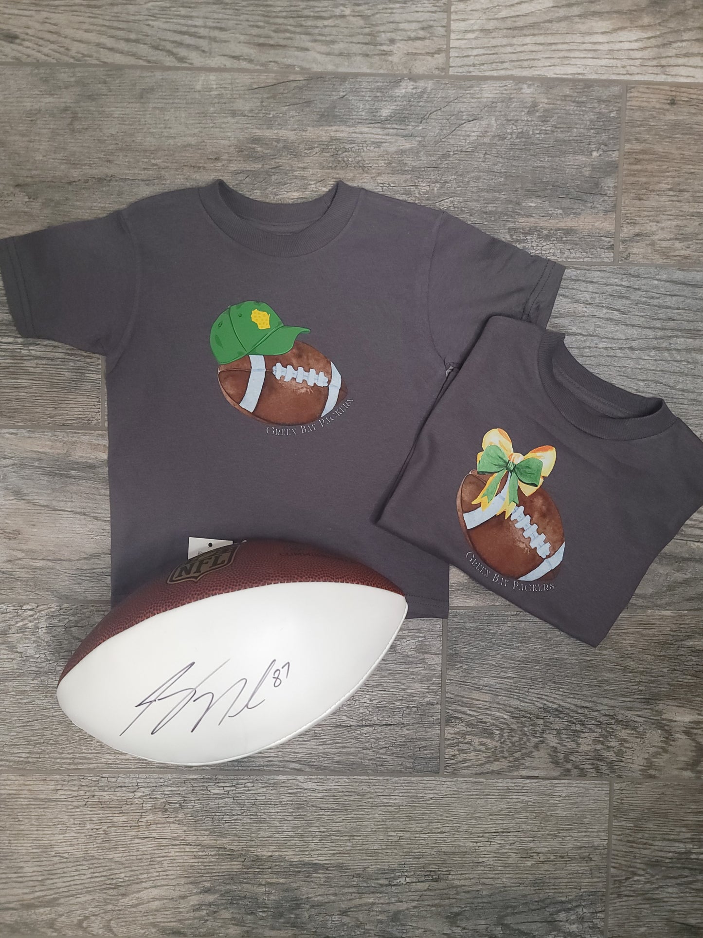 Flat lay of Green Bay Packers Toddler Tee styled with bow, baseball cap, and football, showing full outfit option