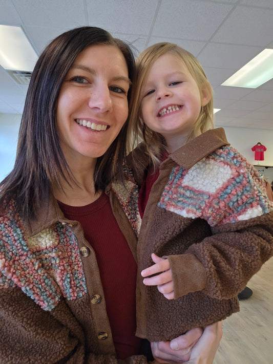 Woman and child wearing matching brown jackets with colorful patterns indoors.