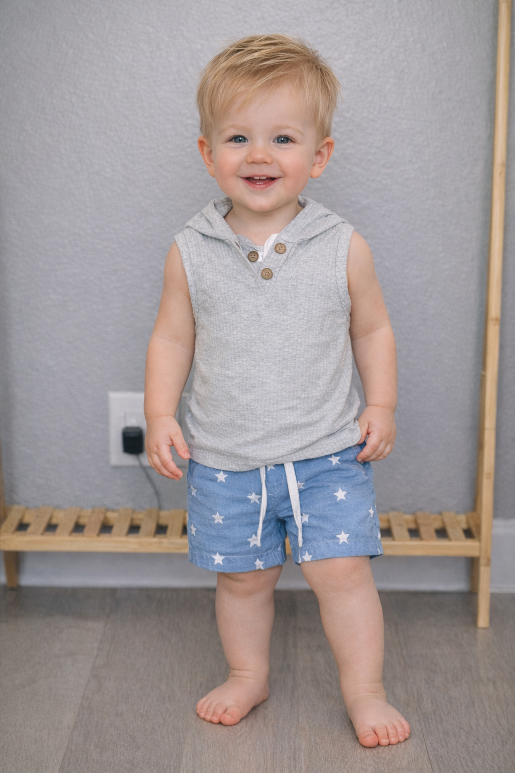 12-month-old toddler boy wearing a gray sleeveless hooded tank top and blue star print shorts