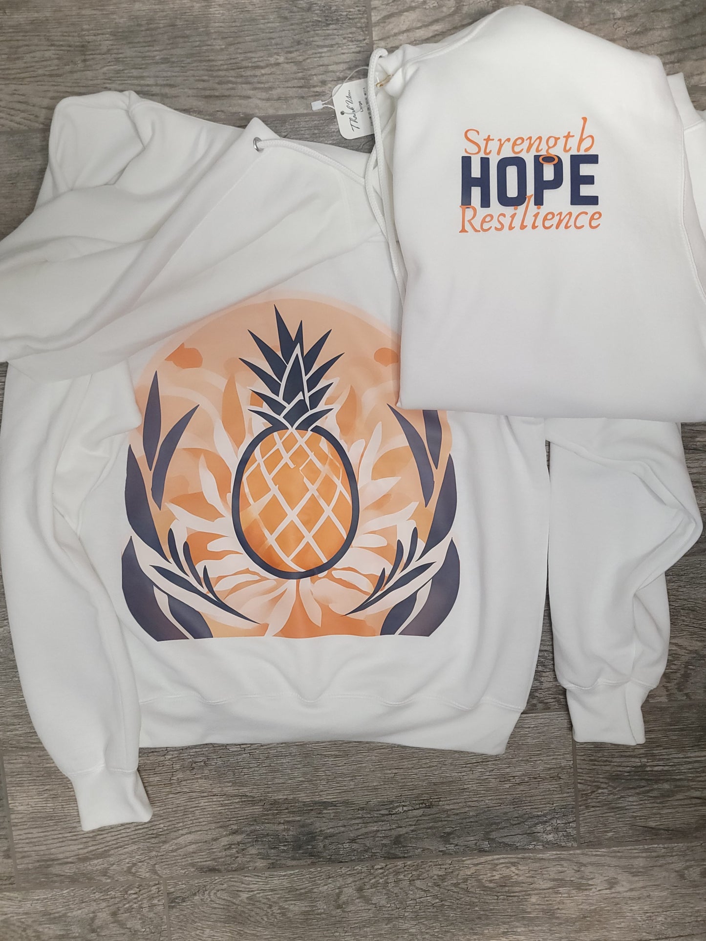Flat lay of H.S.R. Hoodie showing front with pineapple hope graphic and back design, symbolizing infertility awareness and resilience
