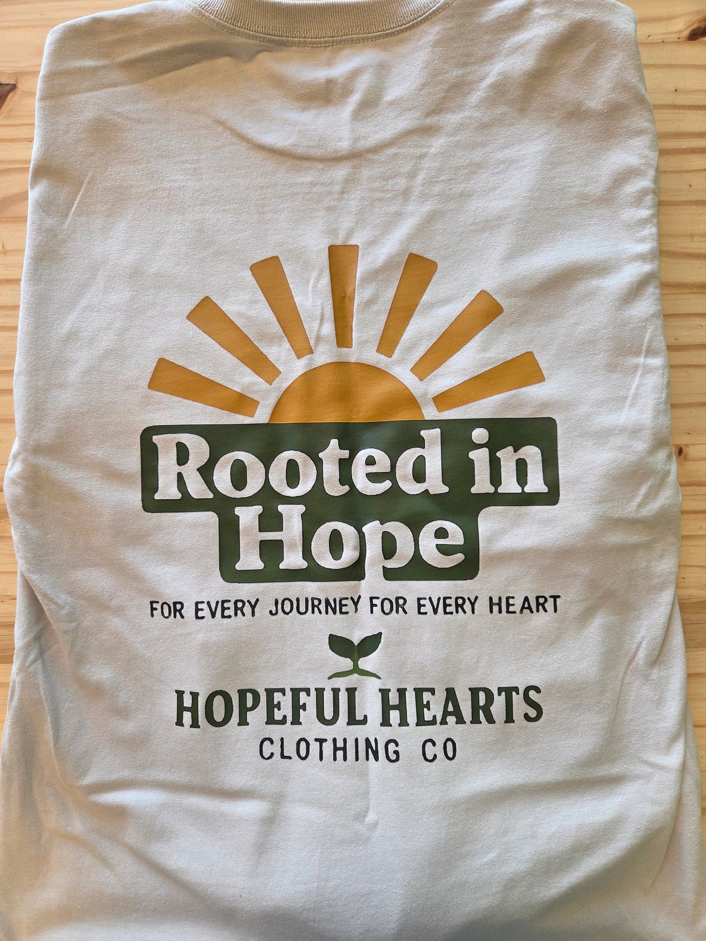 Flat lay of Hopeful Hearts long sleeve tee in dust color, back view showing inspirational quote “Rooted in Hope for Every Journey and Every Heart”