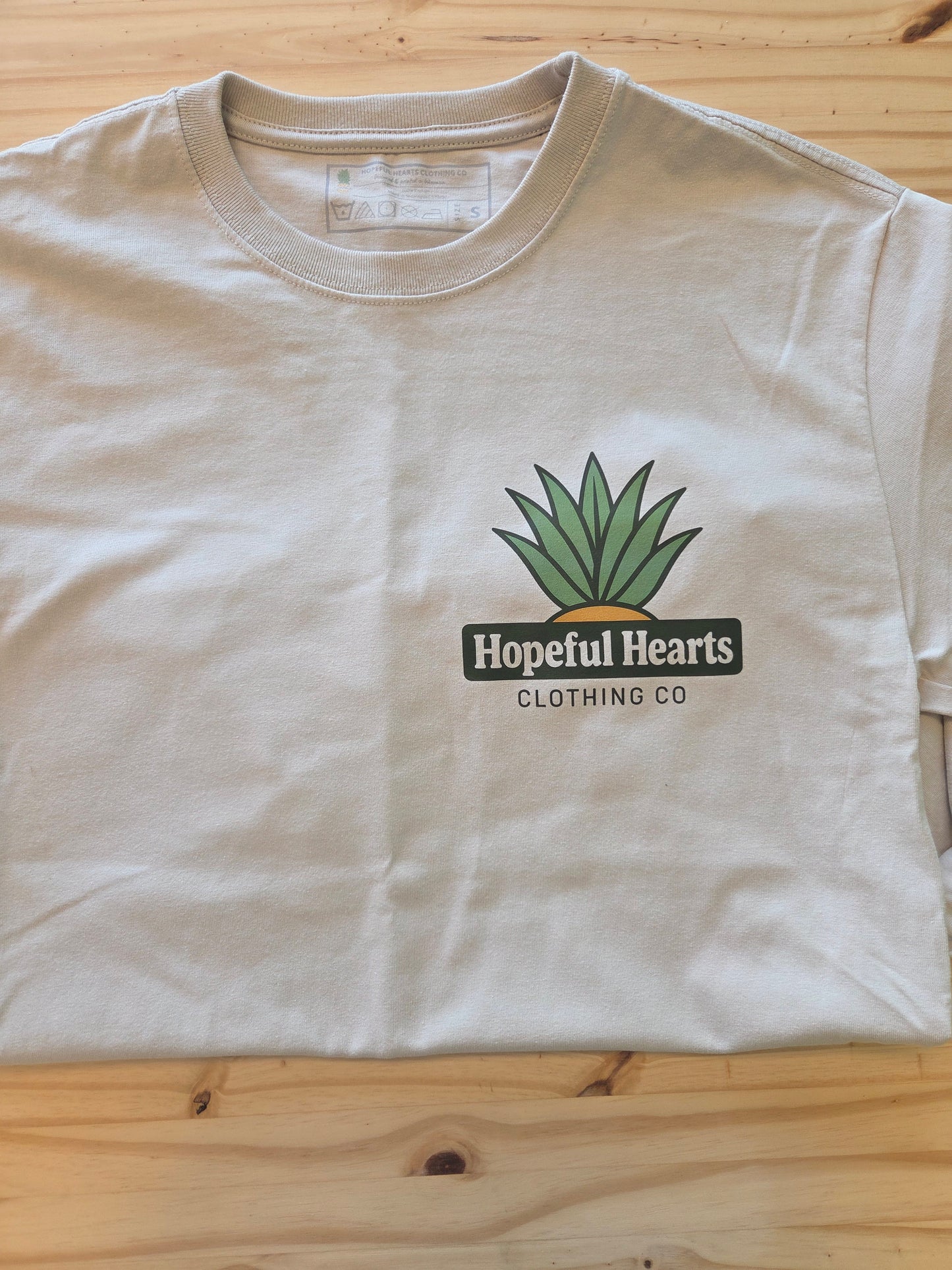 Close-up flat lay of Hopeful Hearts long sleeve tee in dust color, highlighting the front “Hopeful Hearts Clothing Co.” logo