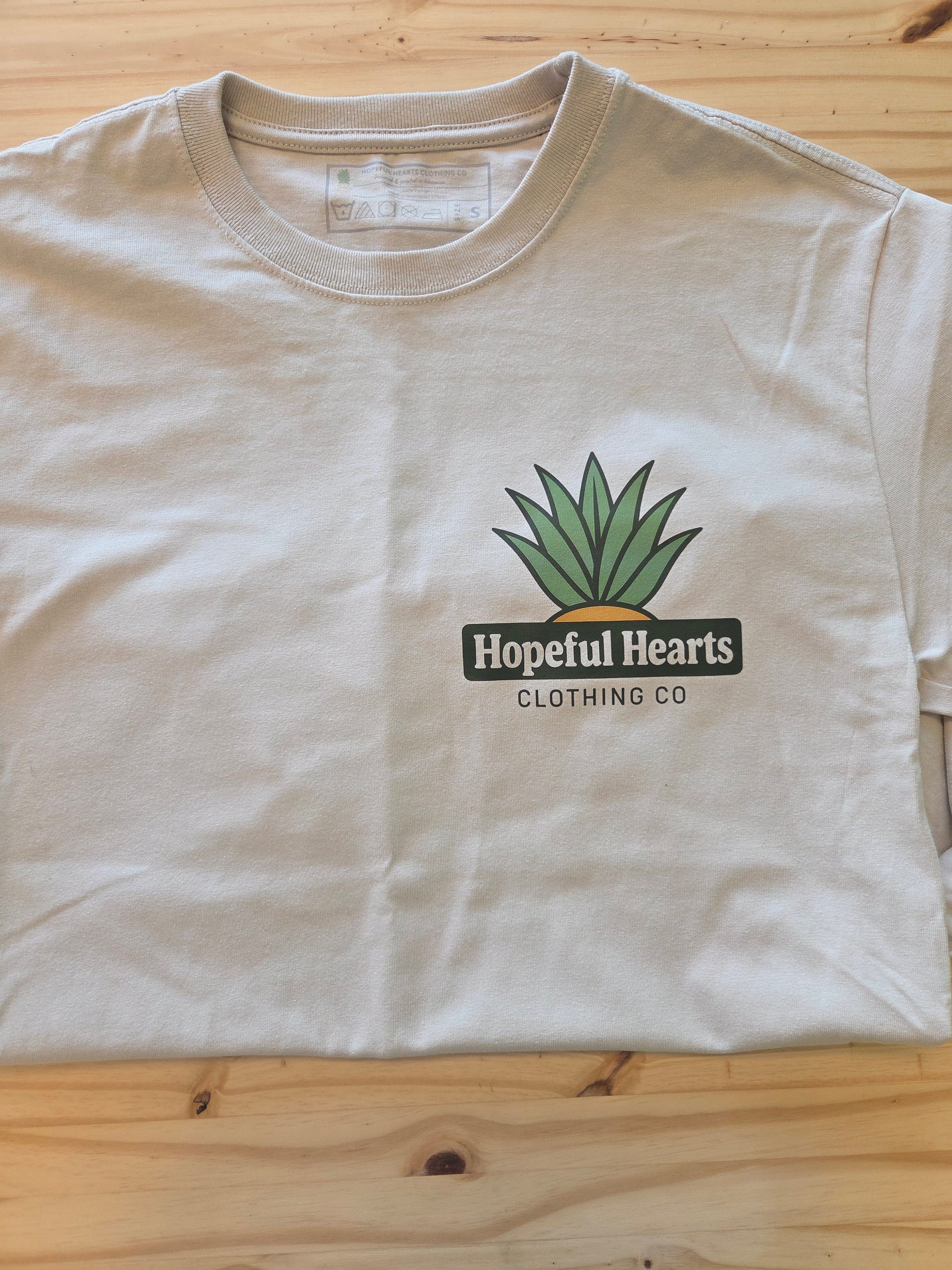 Close-up flat lay of Hopeful Hearts long sleeve tee in dust color, highlighting the front “Hopeful Hearts Clothing Co.” logo