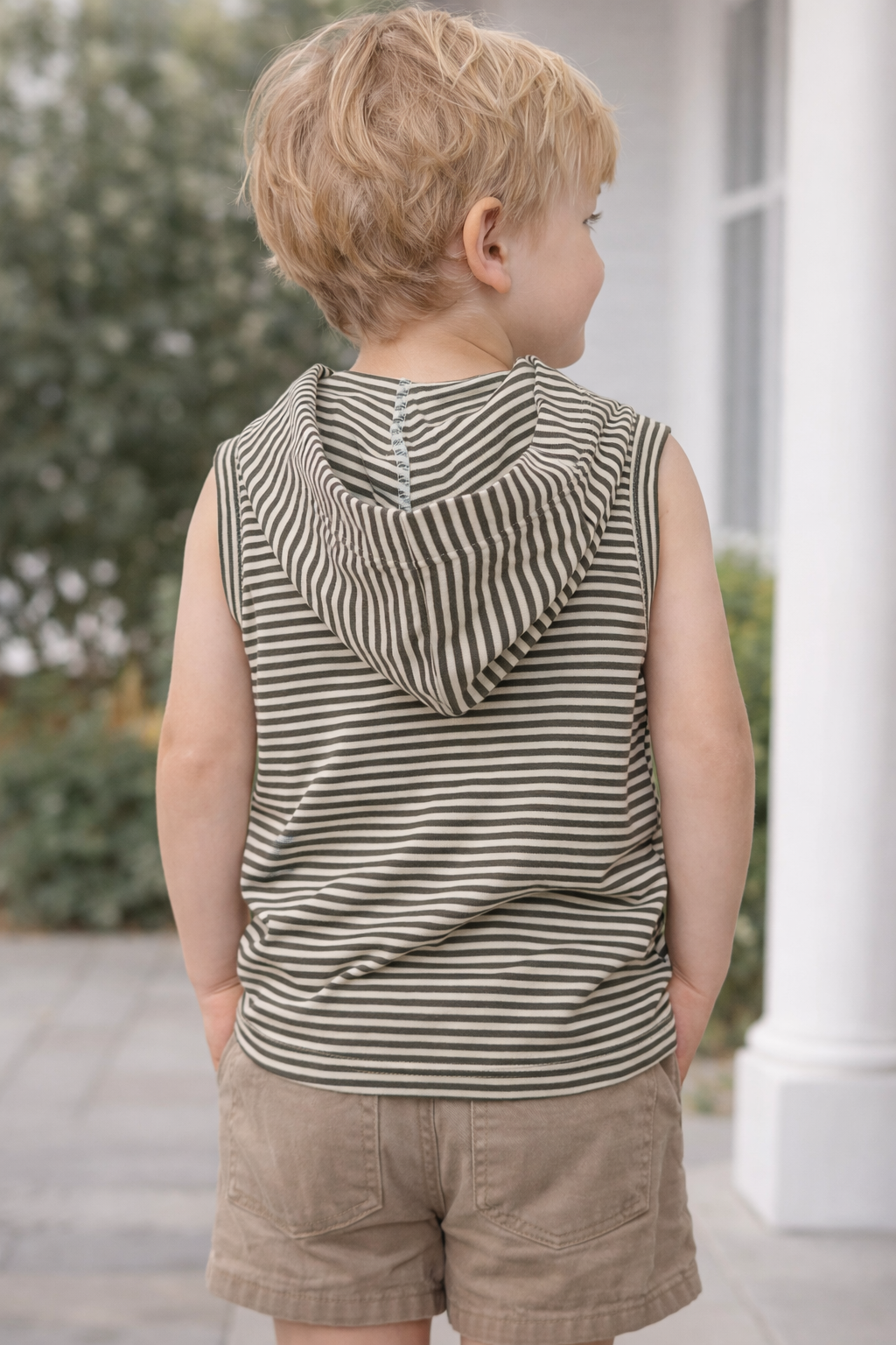 Toddler boy wearing a striped sleeveless hooded tank top, back view showing hood detail and relaxed fit, neutral outdoor setting