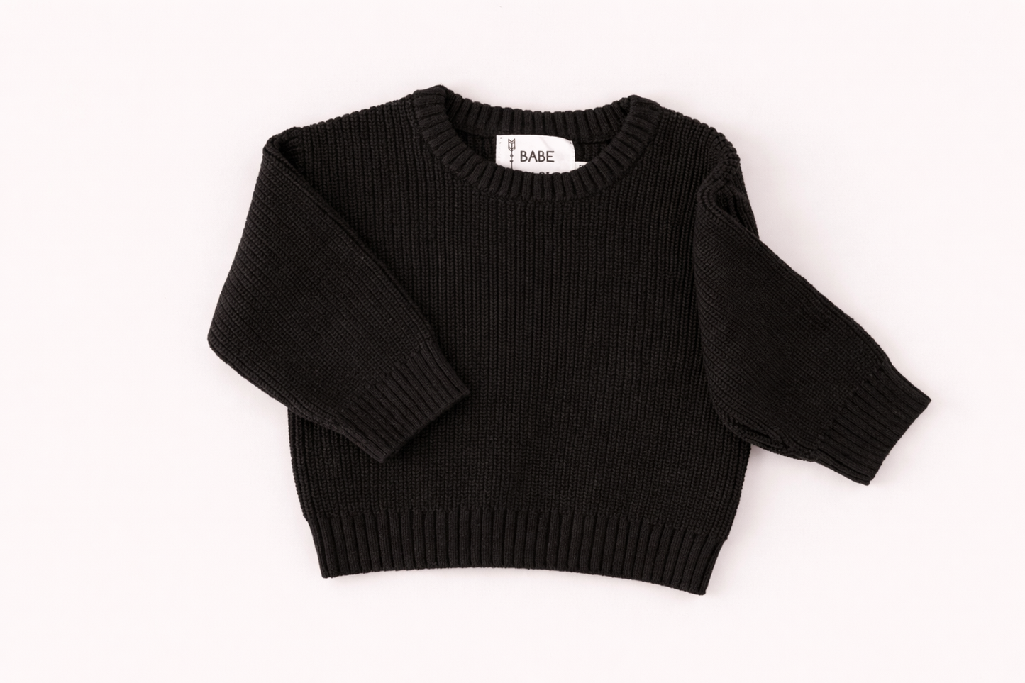 Black knit baby sweater displayed in a clean flat lay, highlighting ribbed neckline, cuffs, and cozy textured fabric
