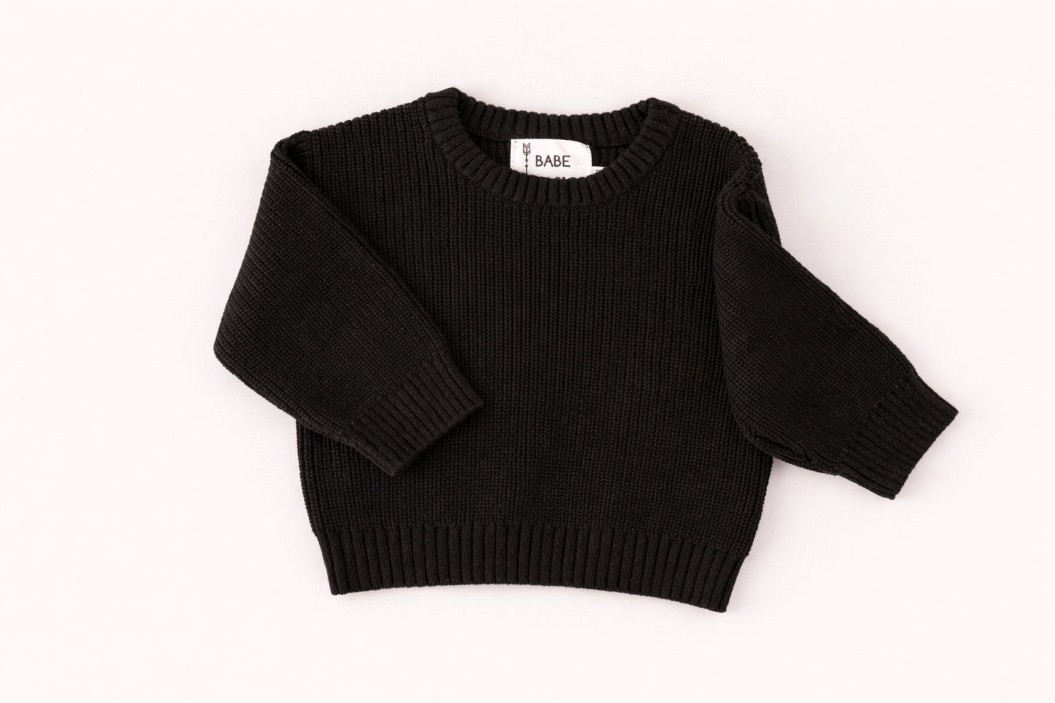 Black knit baby sweater displayed in a clean flat lay, highlighting ribbed neckline, cuffs, and cozy textured fabric