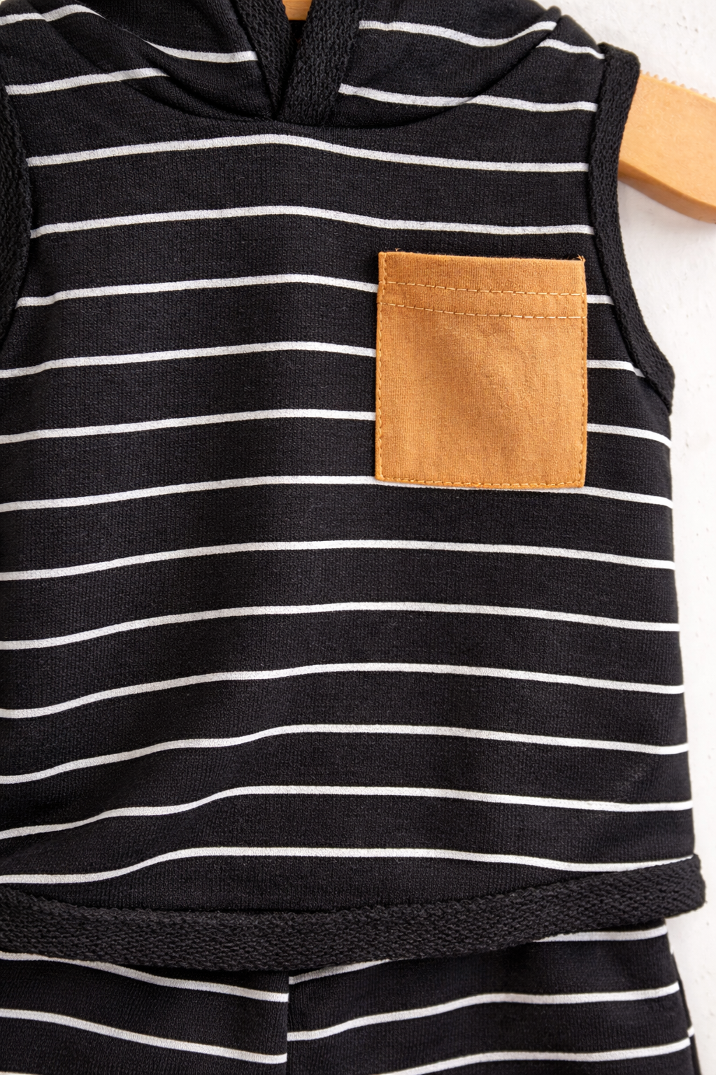 Close-up of black and white striped baby hooded sleeveless top featuring a tan contrast chest pocket, soft textured fabric detail for infant and toddler outfit set
