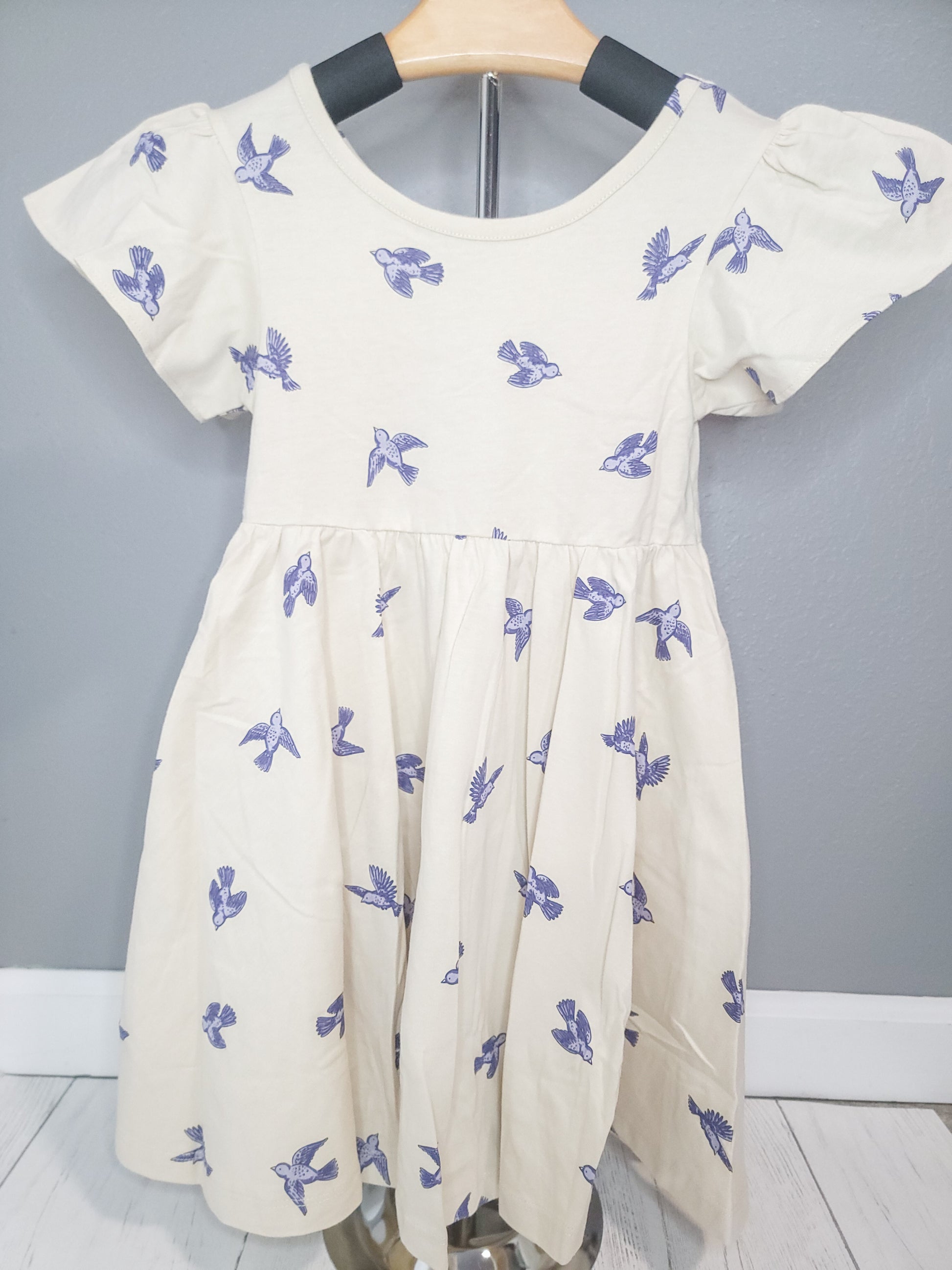 Full view of Bluebird Twirl Dress for toddler girls on rack, highlighting cotton fabric and flutter sleeves