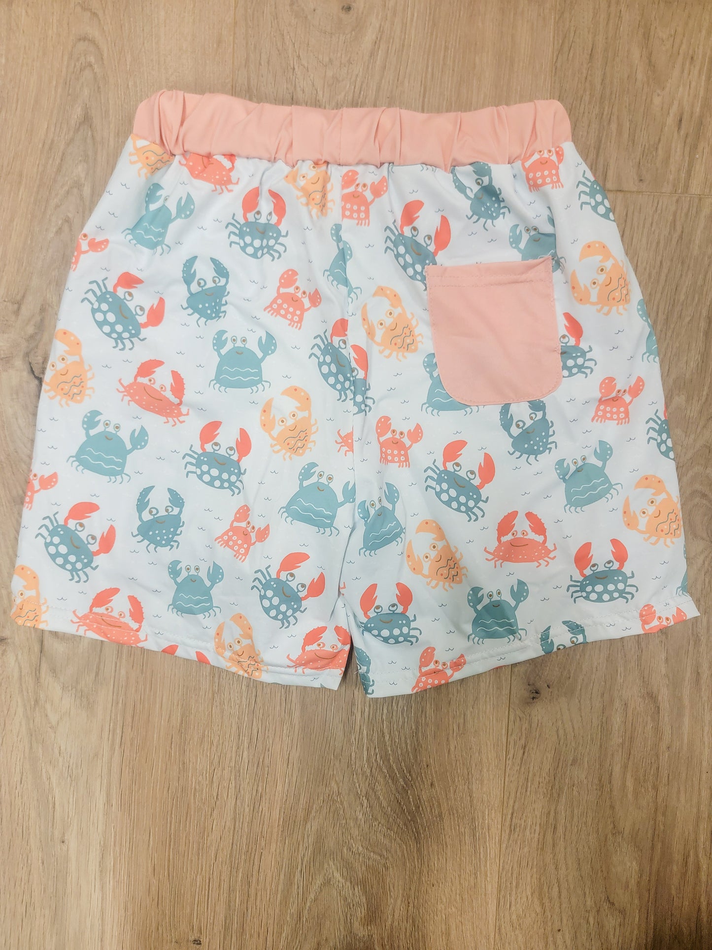 Close-up flat lay of boys crab print swim trunks showing playful crab pattern and adjustable drawstring waistband