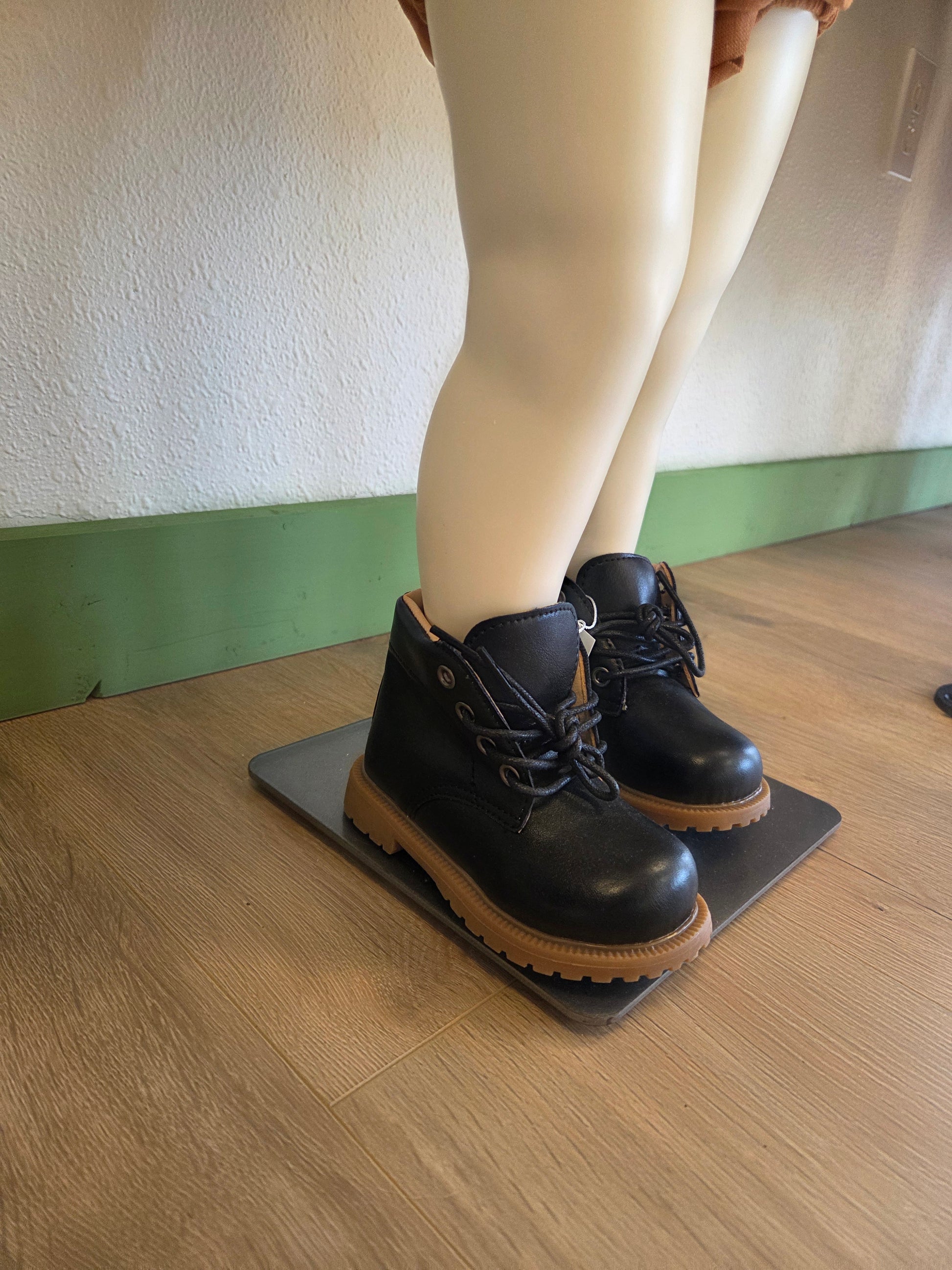 Side view of black unisex toddler and youth combat boots on mannequin, showing silhouette and lace-up detail