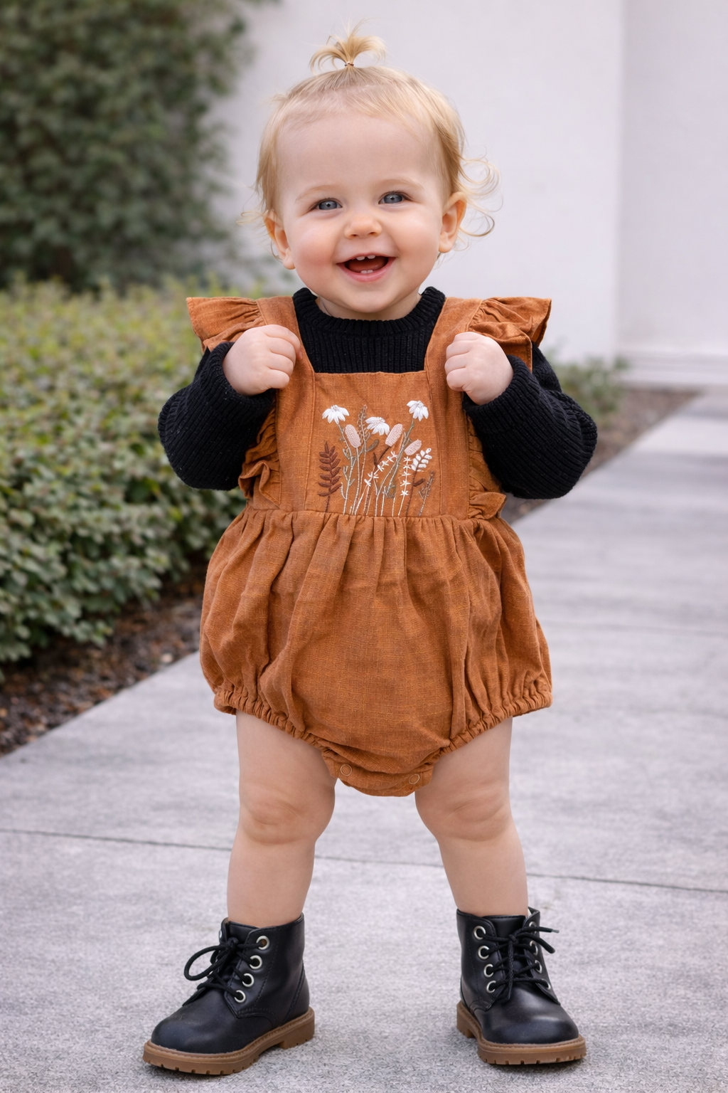 12-month-old baby wearing a rust embroidered romper layered over a black sweater with black lace-up boots, styled as a fall outfit for babies
