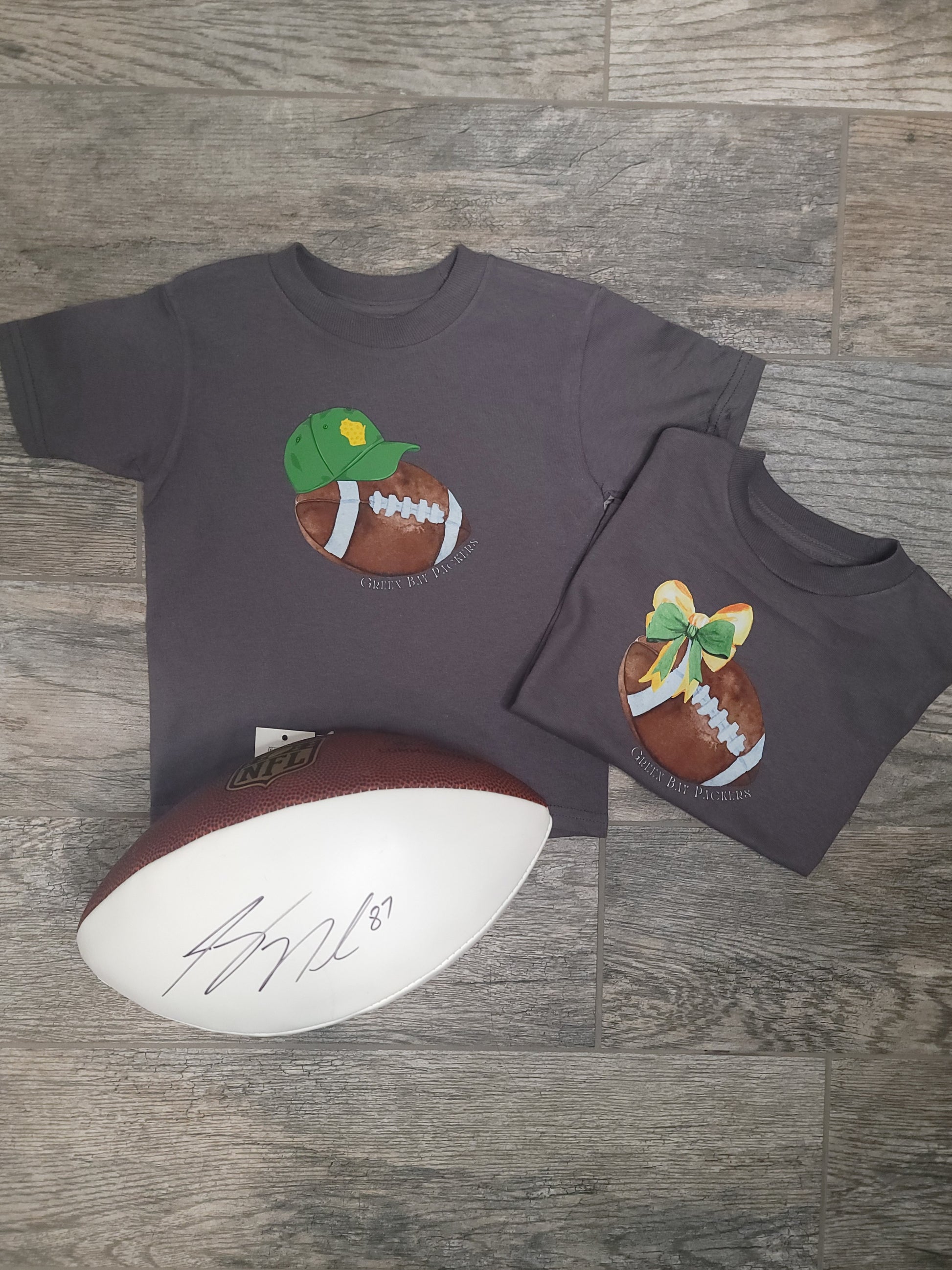 Flat lay of Green Bay Packers Toddler Tee styled with bow, baseball cap, and football, showing full outfit option