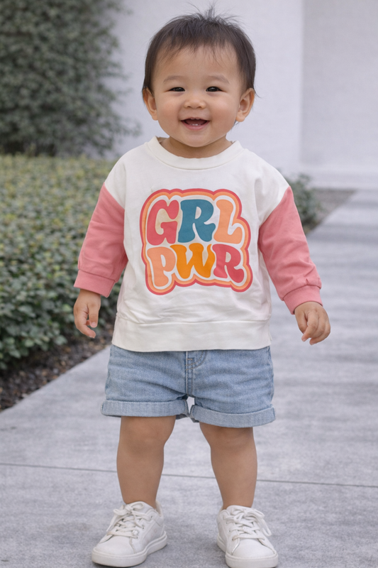 12-month-old toddler model wearing white GRL PWR shirt with pink sleeves, styled on an Asian baby standing outdoors