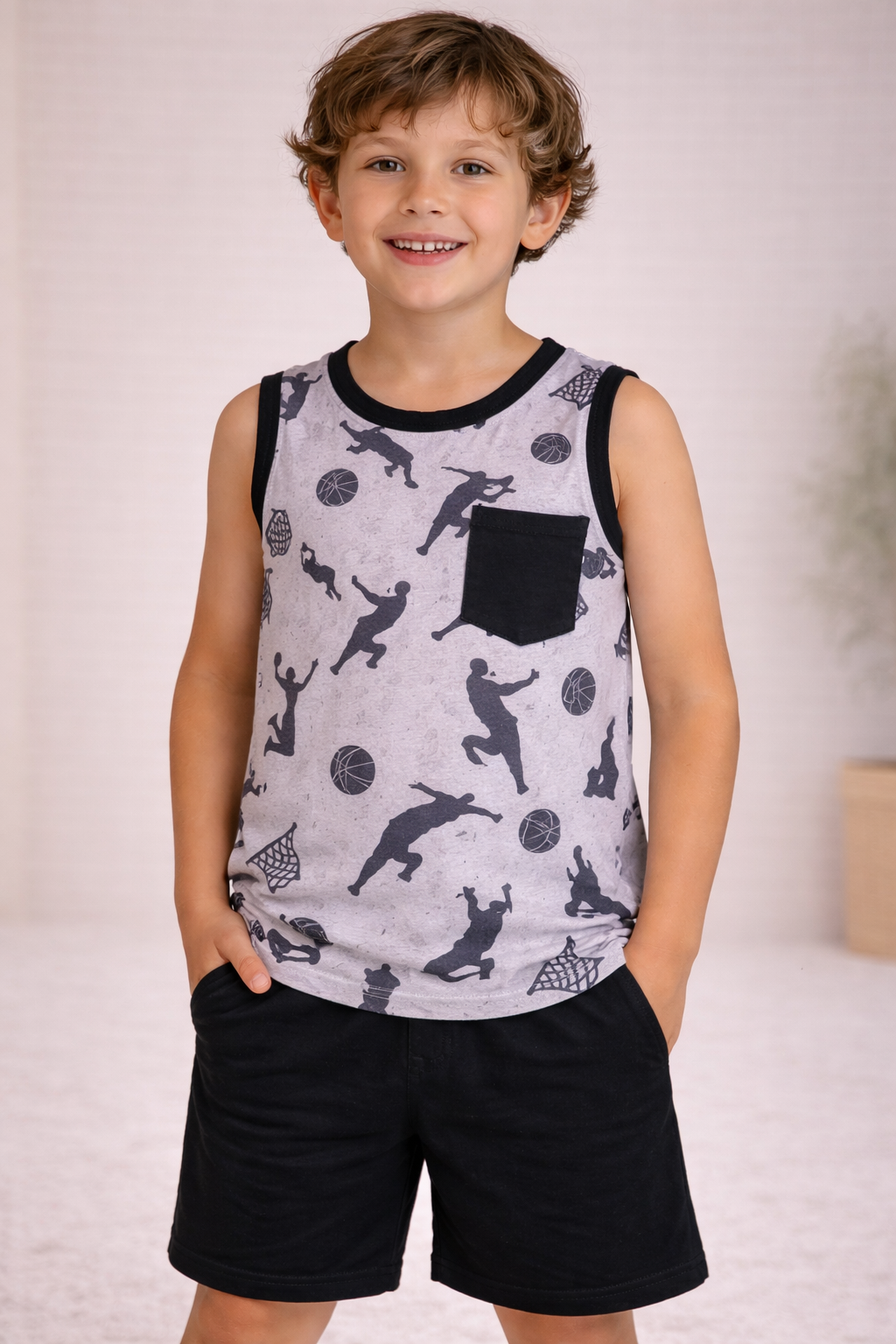 Child wearing a gray basketball silhouette print sleeveless tank with black trim and black chest pocket, paired with solid black shorts, standing in a neutral studio setting.
