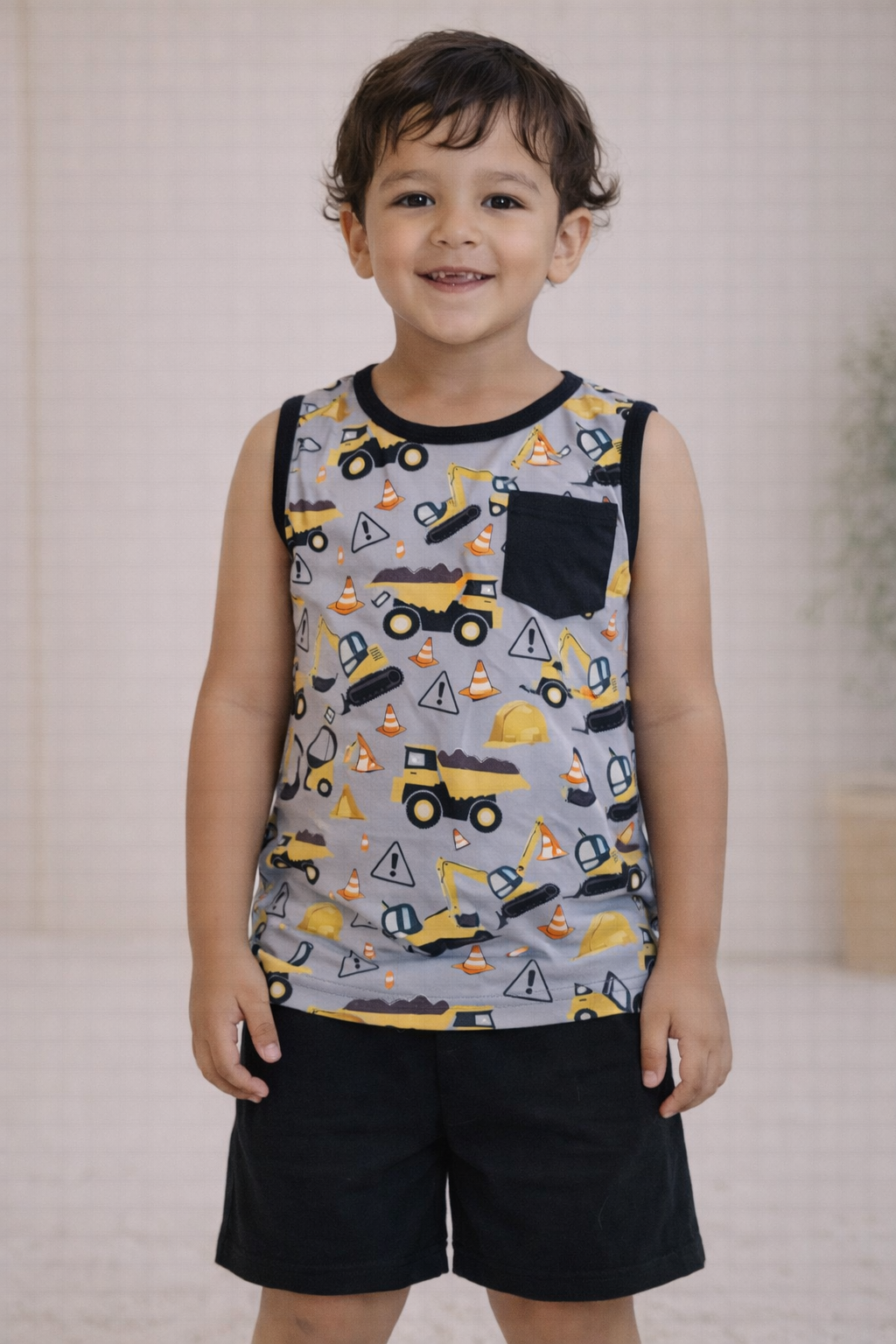 Child wearing a gray construction print sleeveless tank with black pocket detail and solid black shorts, standing in a neutral studio setting