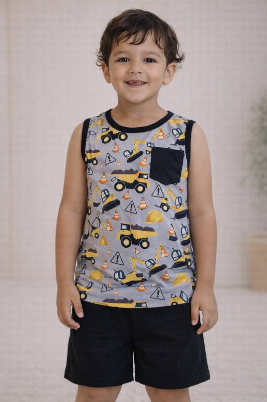 Child wearing a gray construction print sleeveless tank with black pocket detail and solid black shorts, standing in a neutral studio setting