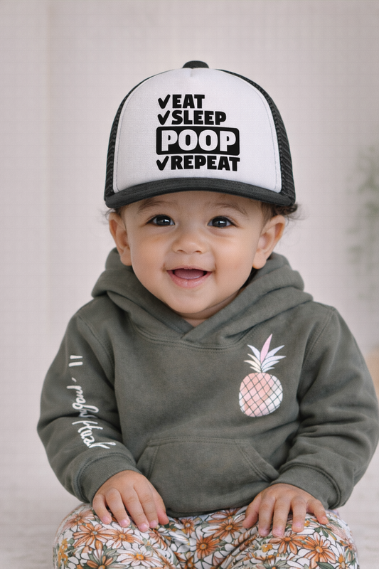 Infant wearing a black and white trucker hat with “Eat Sleep Poop Repeat” text, sitting in a neutral studio setting.