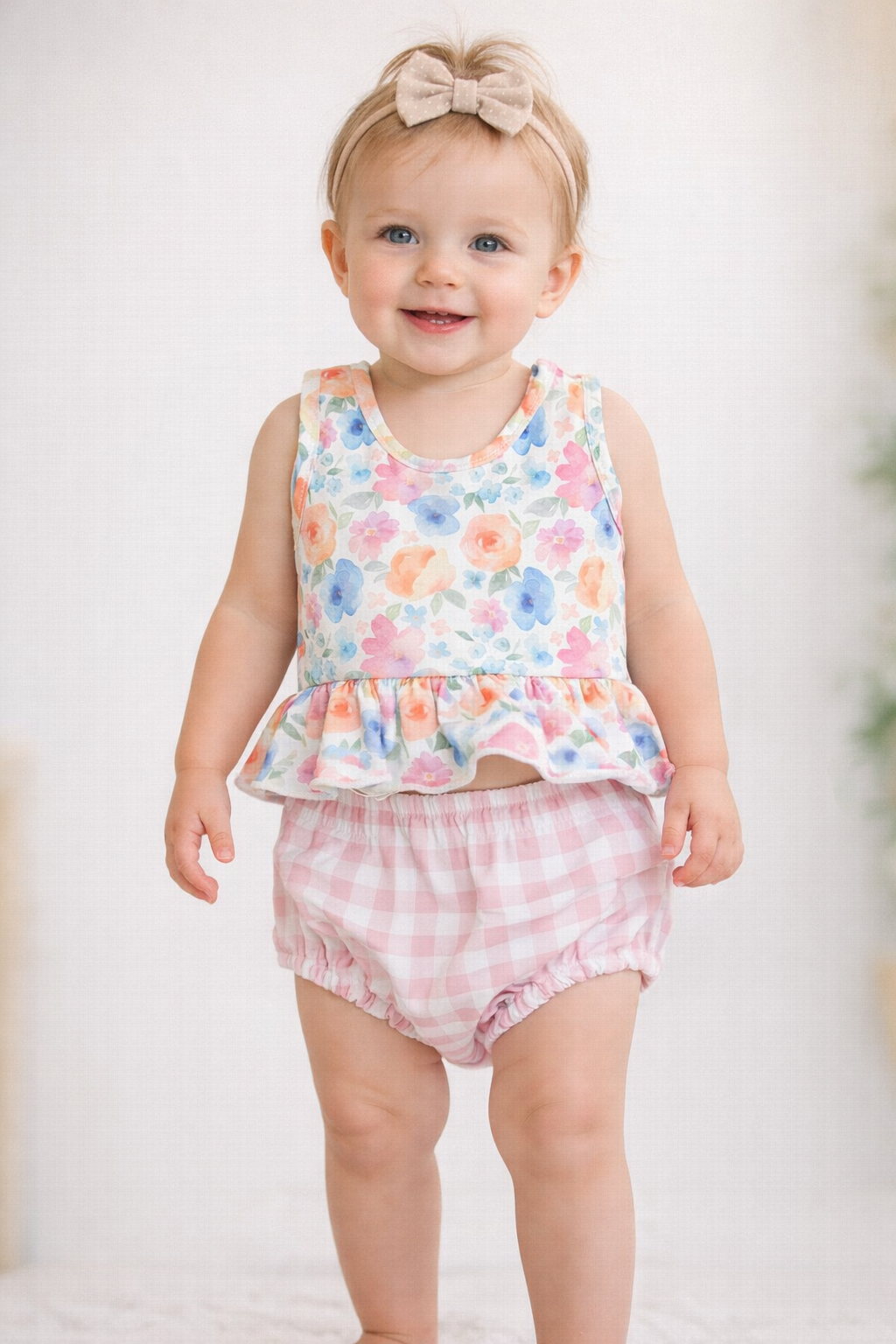Floral peplum tank top with pink gingham bloomer bottoms laid flat on a wood background, girls two-piece outfit.