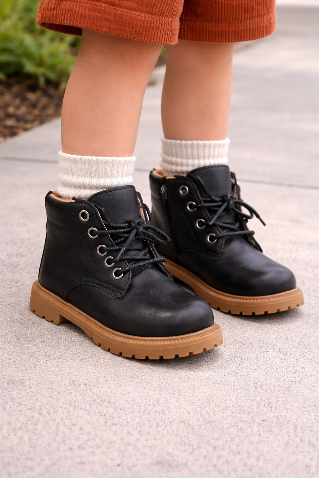 Toddler wearing black combat boots with tan soles, styled on a child model with the boots as the focal point