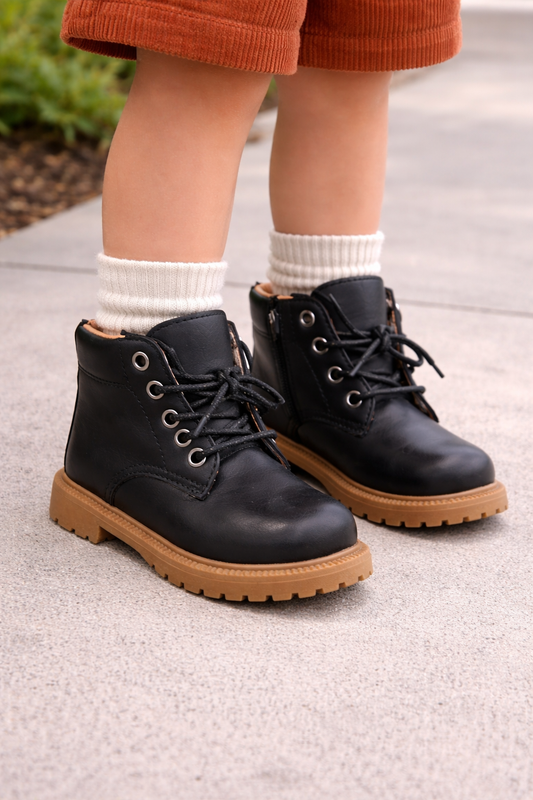Toddler wearing black combat boots with tan soles, styled on a child model with the boots as the focal point