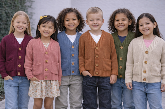 Six diverse children wearing youth size 6 knit cardigans in maroon, salmon, blue, orange, olive green, and cream, standing side by side outdoors.