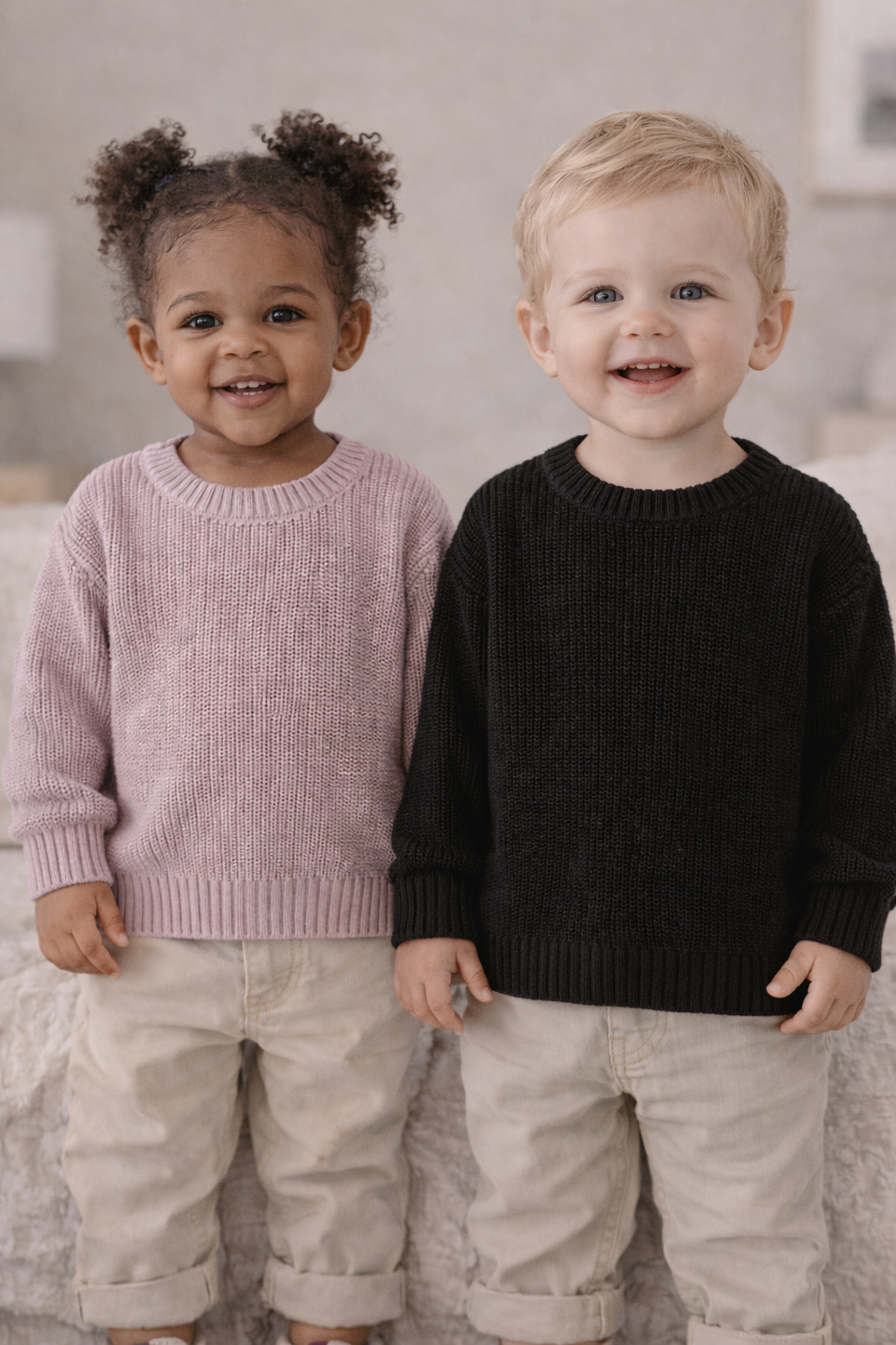 Two toddlers wearing knit sweaters in soft pink and black, shown on models to highlight fit, texture, and everyday wear