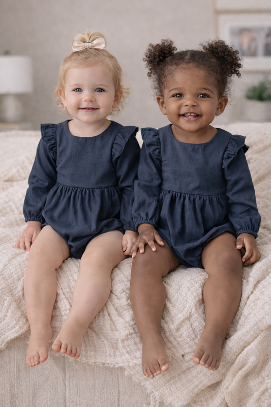 Two toddlers wearing navy ruffle shoulder rompers, shown on models in size 18–24 months to display full outfit fit and details