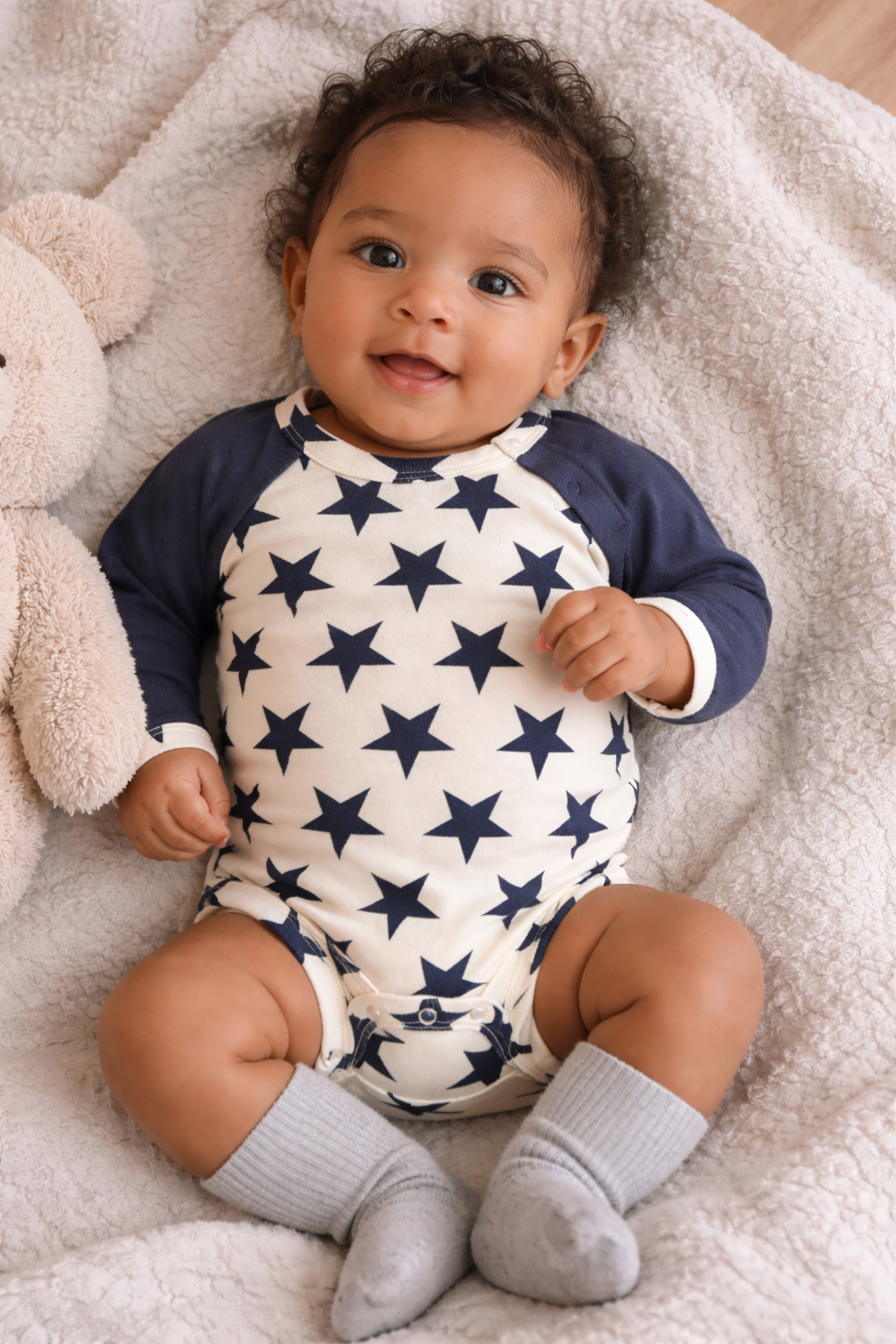 Smiling infant wearing a cream and navy star long sleeve onesie, shown on a baby model in a cozy lifestyle setting