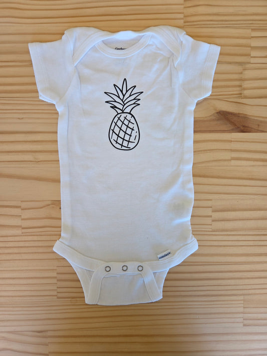 Flat lay of white baby onesie size 3–6 months with black pineapple print, symbolizing infertility awareness, rainbow babies, and hope
