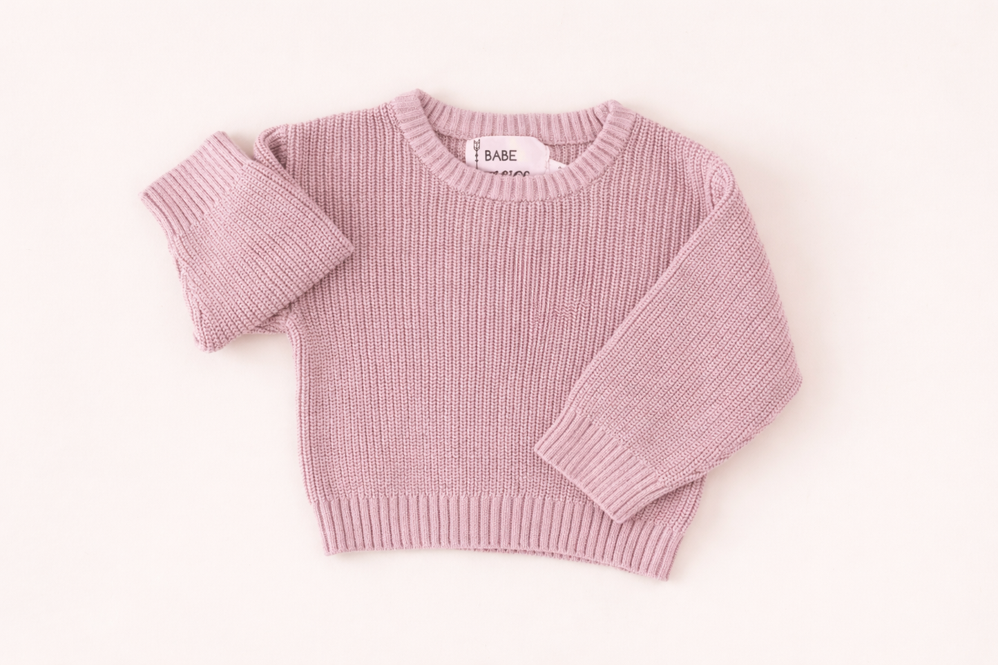 Soft pink knit baby sweater displayed in a clean flat lay, highlighting ribbed neckline, cuffs, and cozy texture