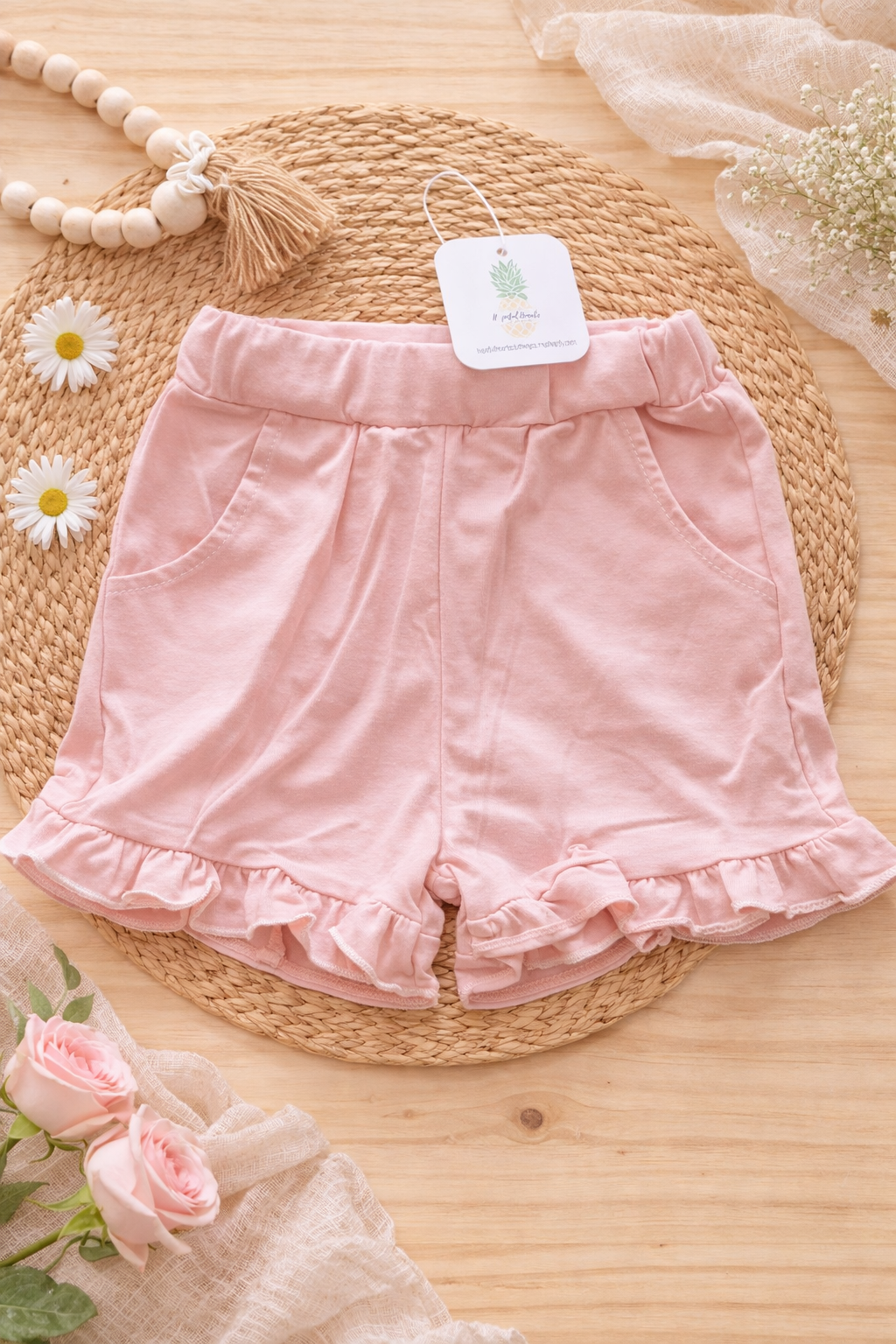 Soft pink ruffled baby shorts styled in a flat lay, featuring elastic waist and feminine ruffle trim