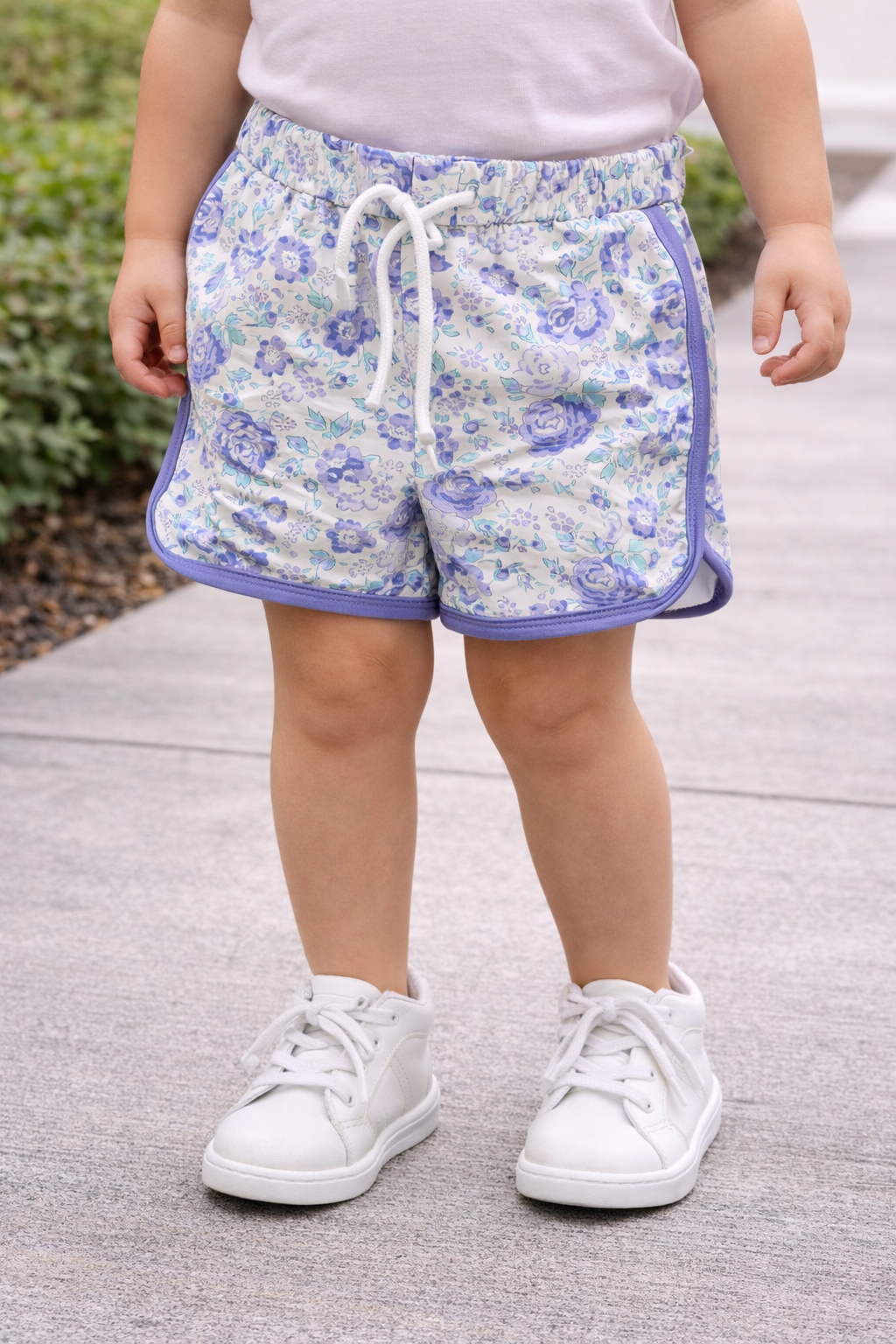 Toddler wearing purple and blue floral drawstring shorts with white sneakers, shown in a lifestyle fit to highlight comfort, fit, and everyday wear.