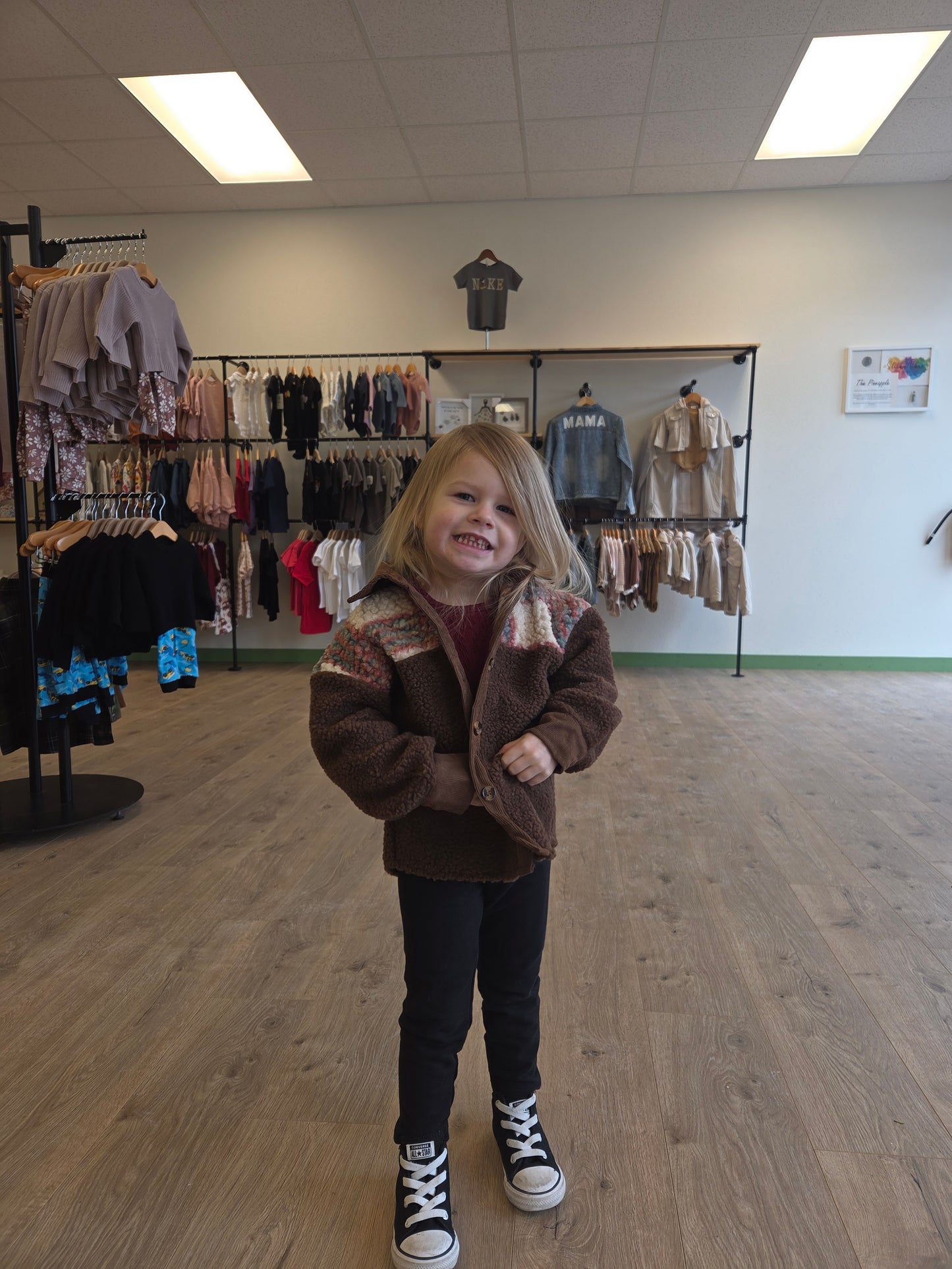 Person wearing a brown coat standing in a room with a rack of clothes.