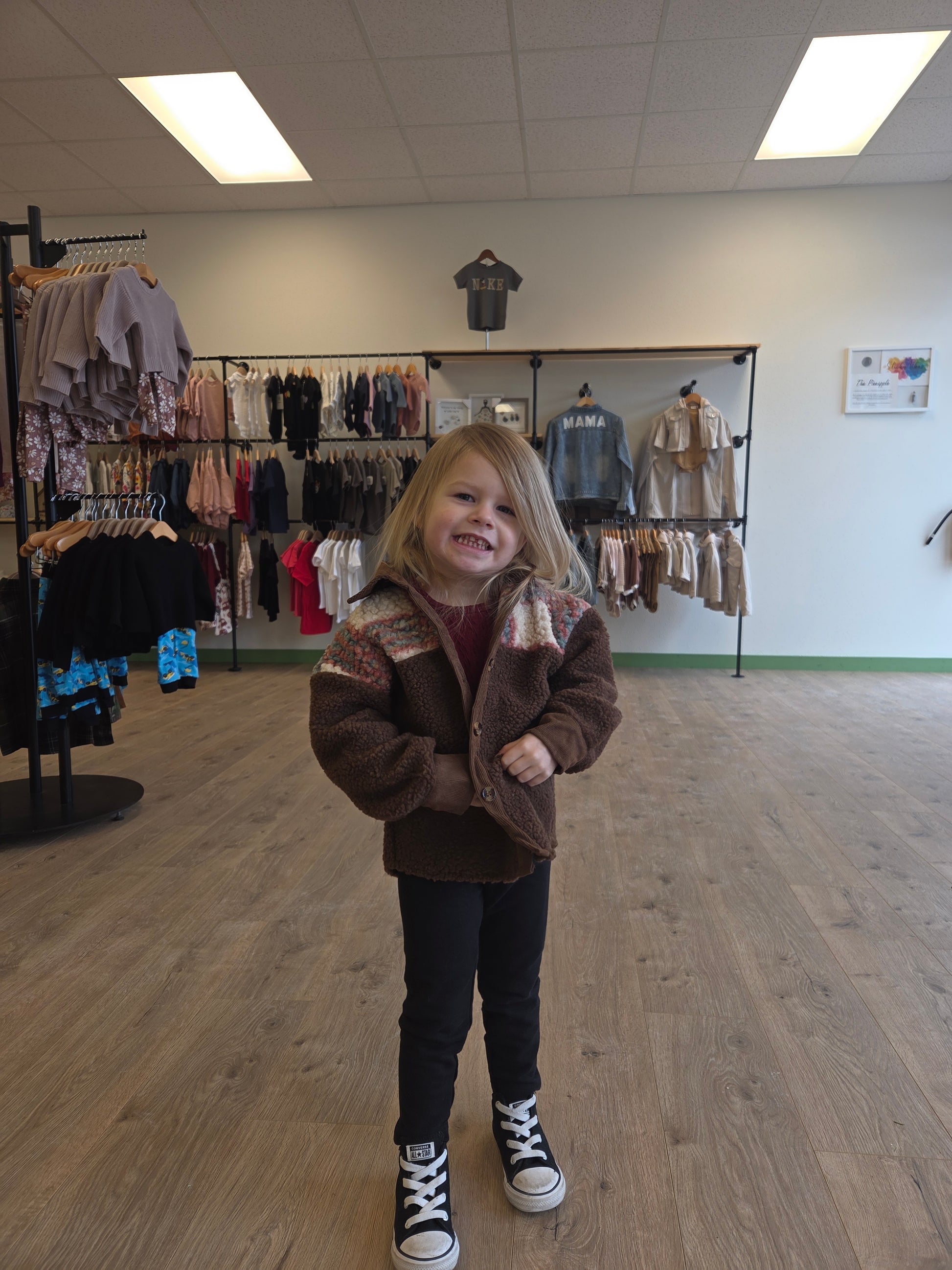 Person wearing a brown coat standing in a room with a rack of clothes.