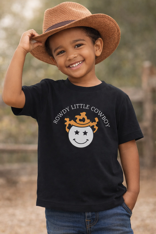 Toddler wearing black “Rowdy Little Cowboy” graphic t-shirt with cowboy hat in western-inspired setting
