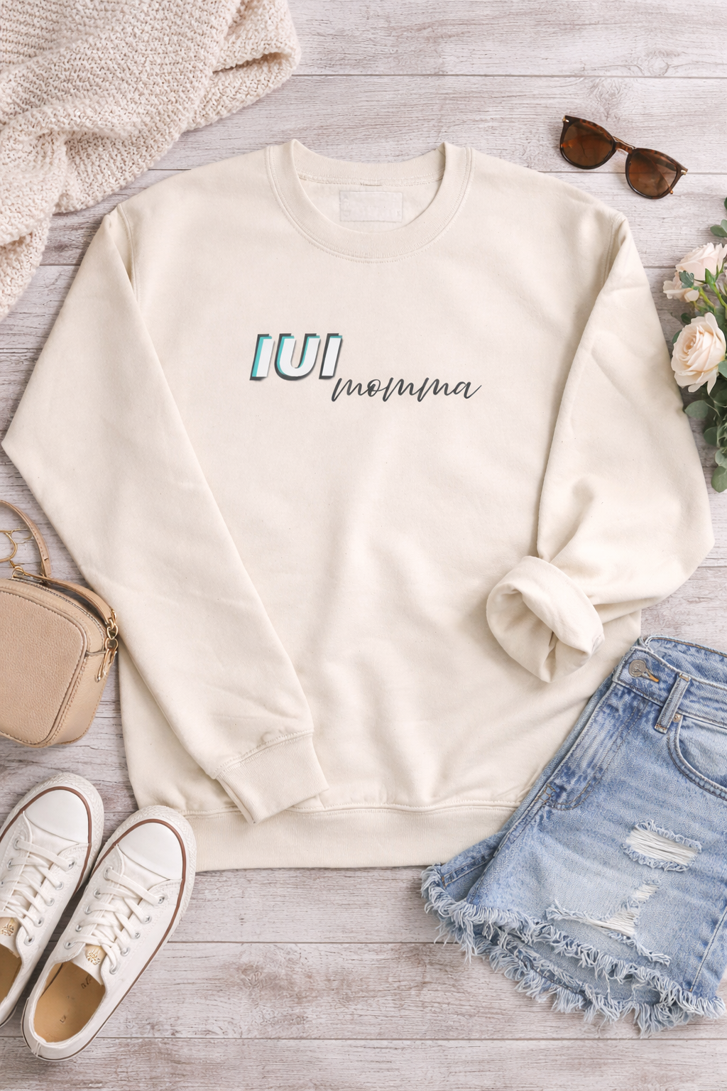 Flat lay of cream UI Momma sweatshirt styled with denim shorts and neutral accessories, women’s boutique appare