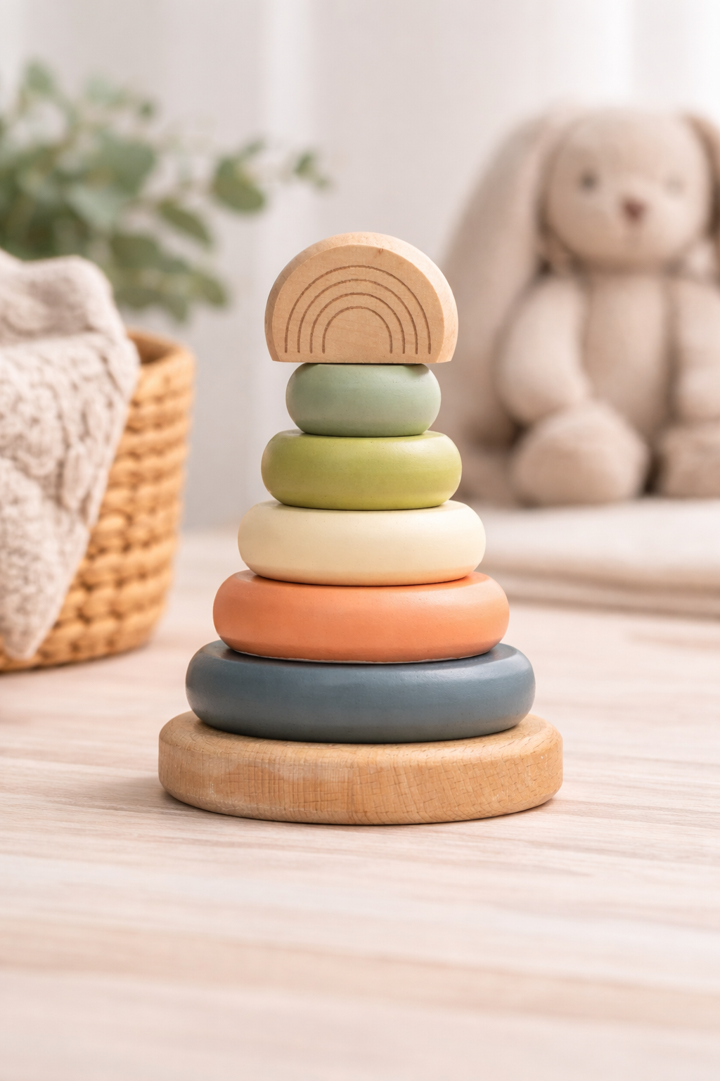 Neutral wooden stacking rainbow tower toy with soft earth-tone rings and engraved rainbow top, styled in a modern nursery setting